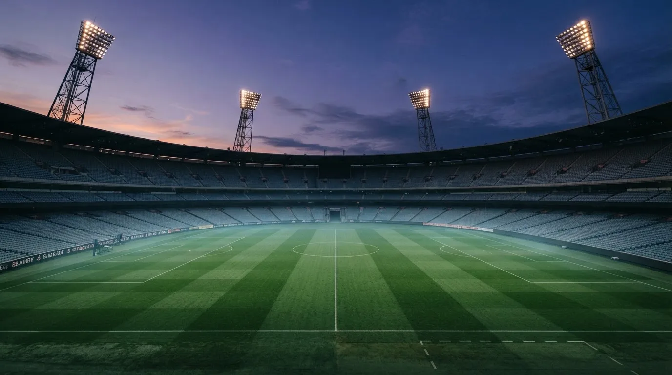 An empty football stadium with floodlight masts at dusk