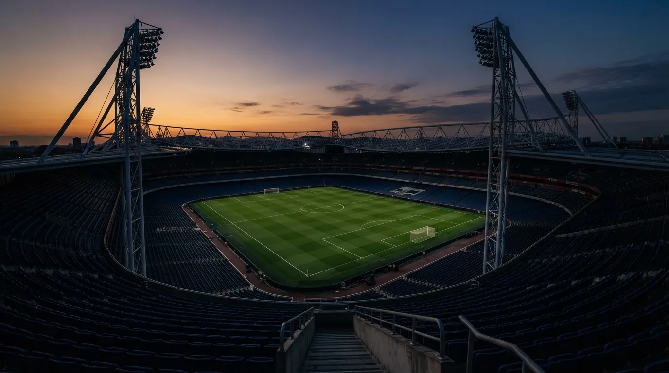 An empty football stadium with floodlight masts at dusk