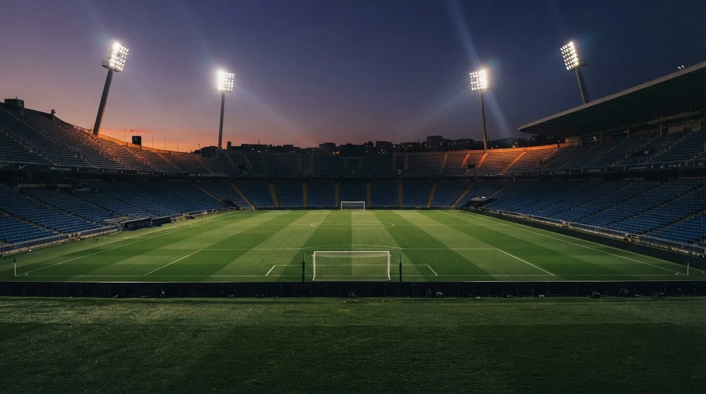 An empty football stadium with floodlight masts at dusk