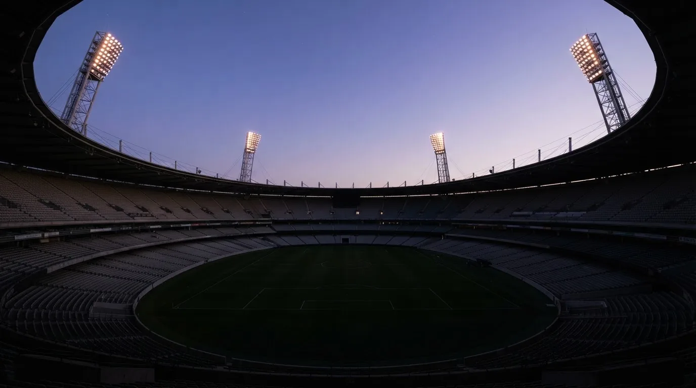 An empty football stadium with floodlight masts at dusk