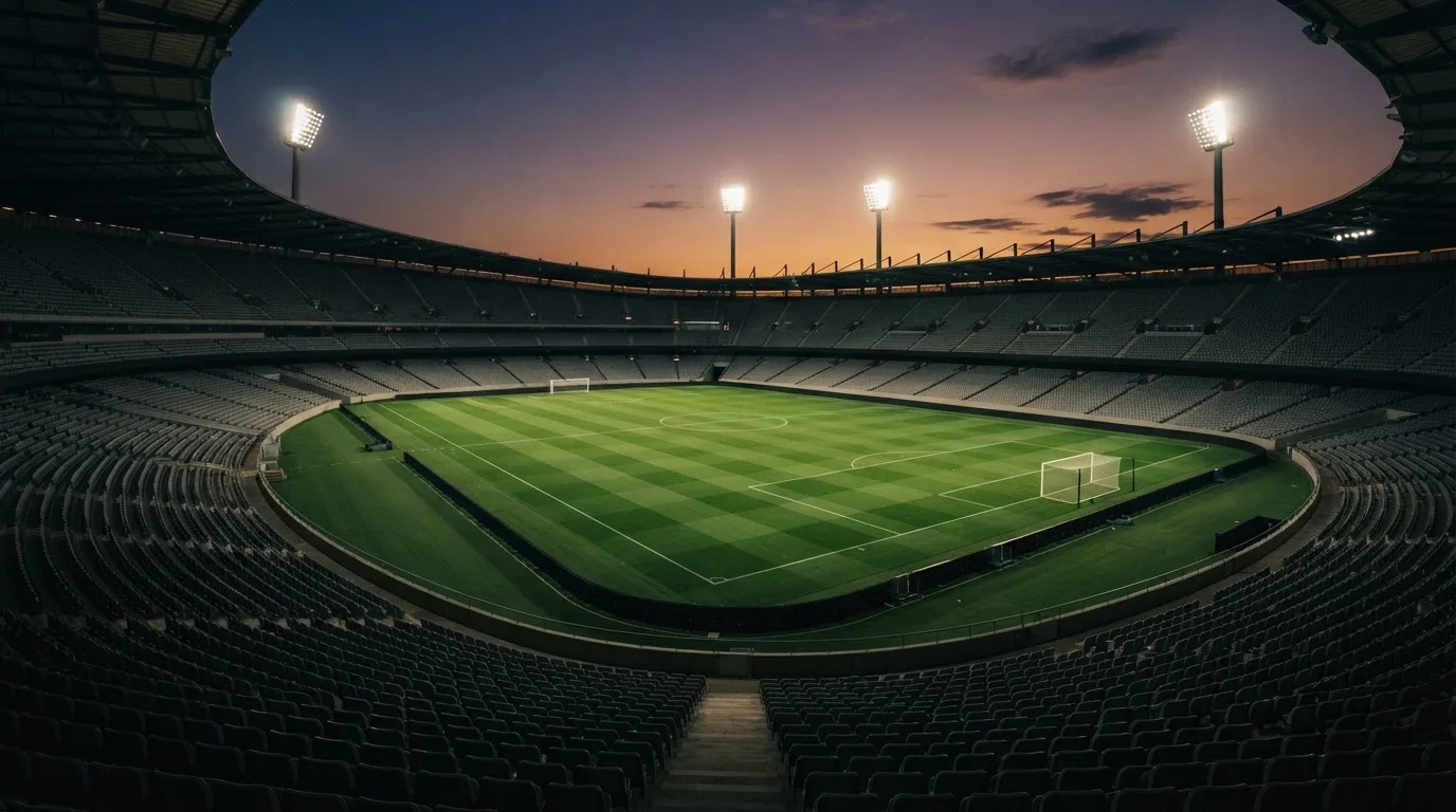 An empty football stadium with floodlight masts at dusk